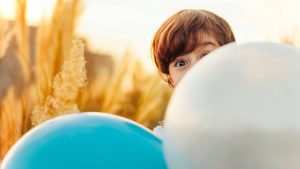 ein Kind im Kornfeld schaut hinter zwei Luftballons hervor