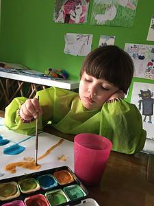 Kind malt Wasserfarbe, dabei legt er den Kopf auf seiner Hand ab