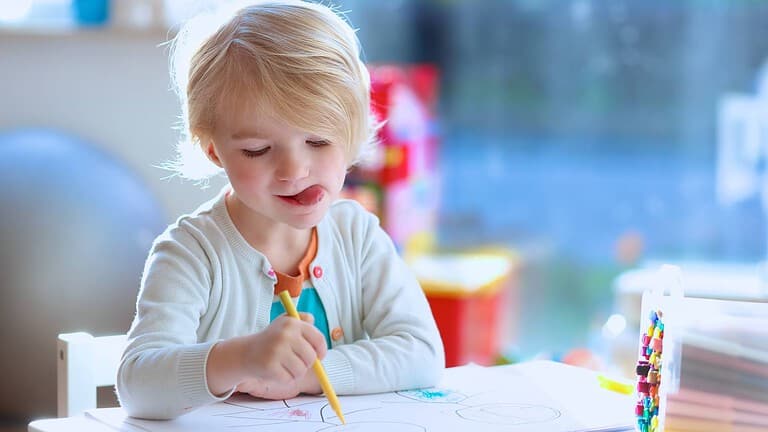 ein Kind malt mit bunten Filzstiften und streckt dabei vertieft die Zunge raus