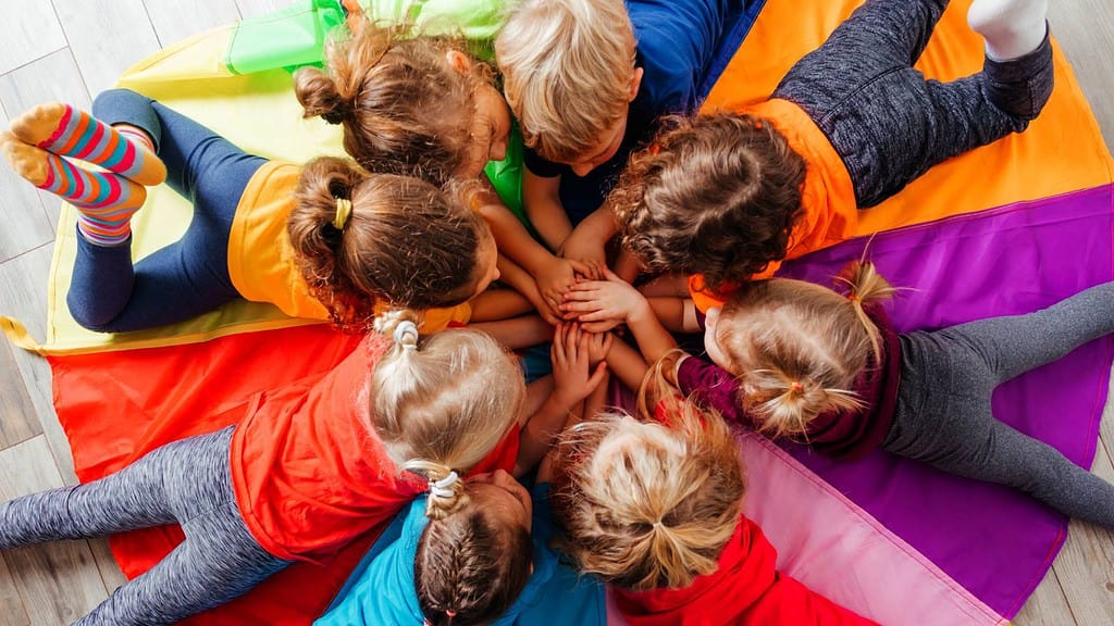 Kinder liegen auf einem bunten Schwungtuch, ihre Hände berühren sich in der Mitte