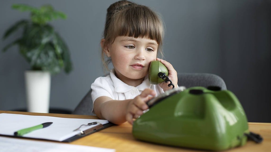 ein Kind sitzt am Schreibtisch und telefoniert mit einem Kabeltelefon